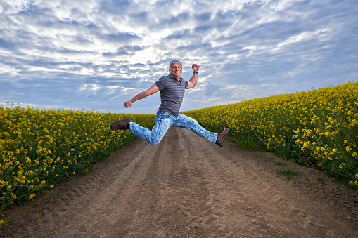 Happy farmer jumping for joy in his canola field at sunset