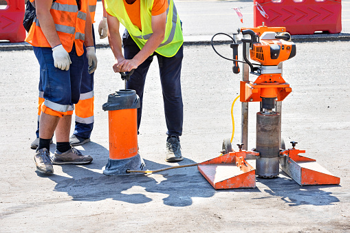 Road workers use a core drill to extract cores from an asphalt pavement during road repairs. Copy space.