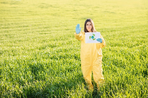 Person in overalls holds paper with a call to save the planet while standing on green field on sunset and the other hand shows a gesture to stop and not pollute the planet. Concept of bad ecology and environmental protection