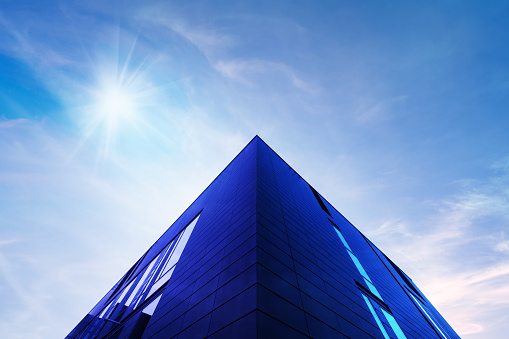 Abstract modern architecture detail with copy space. Blue sky, clouds and sunshine. Upward view from the ground.