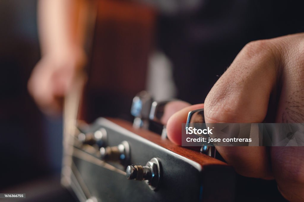 side view man tuning acoustic guitar with hand on headstock in foreground side view man tuning acoustic guitar with hand on headstock in foreground and blurred guitarist in background with copy space. 30-34 Years Stock Photo