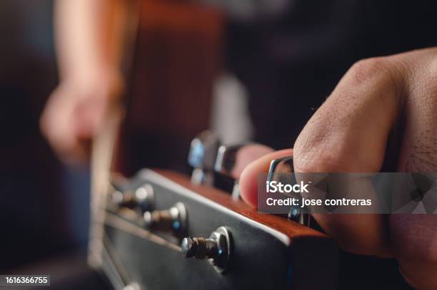 Side View Man Tuning Acoustic Guitar With Hand On Headstock In Foreground Stock Photo - Download Image Now
