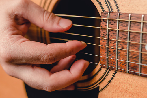 detail caucasian male hand playing acoustic guitar strings, at the level of the mouth of the acoustic box of the guitar.