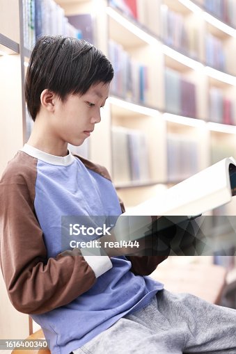 istock Cute boy reading book in library 1616400340