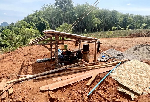 a photography of a small shelter with a roof and a stove, lumbermill with a wooden shelter and a pile of wood.