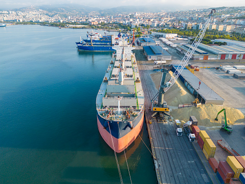 Aerial drone view above sea port. Cargo vessel is loading containers and bulk. Professional business logistics and transportation of cargo ship.