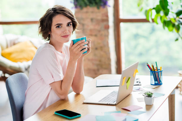 photo de jeune femme mignonne bob cheveux bruns porter rose élégant t-shirt tenir coupe préférée cappuccino pause café avec netbook isolé à l’intérieur - women computer home interior brown hair photos et images de collection