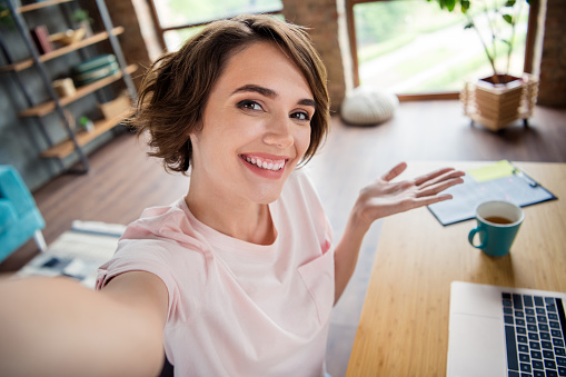 Selfie photo portrait of young friendly businesswoman office manager entrepreneur show her cappuccino isolated over apartment background.