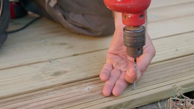 Male builder using drill to screw the screws off the timber