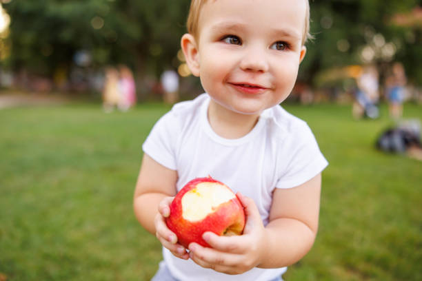 Portrait of a baby with a red apple. Child smiles and looks at the camera