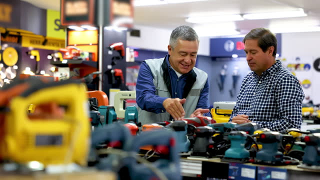 Male customer talking to salesman about an electric hand tool asking him the differences at a hardware store