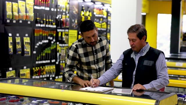 Adult customer checking an order with mature salesman at a hardware store while pointing at the retail display