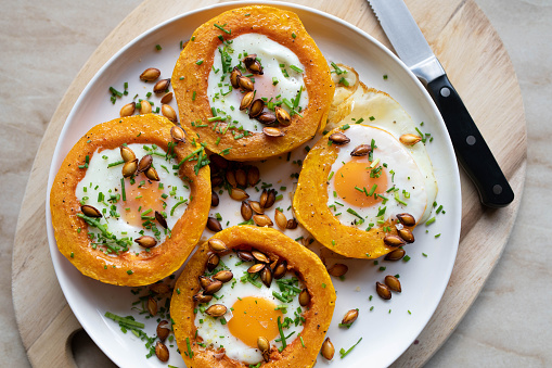 Gluten free and vegetarian, dinner, lunch or breakfast. Suitable for low carb or ketogenic diet. Oven baked pumpkin with fried eggs, seeds and herbs on a plate from above. Zero Waste food