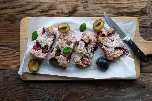 Delicious juicy plum cake or pie with crumble. Traditional german cake. Served ready to eat and sliced on a rustic and wooden cutting board from above.