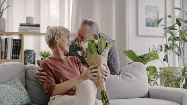 Gift surprise, mature or happy couple with flowers in home on a marriage anniversary celebration on holiday. Wow, present or romantic senior man talking, bonding or giving woman a bouquet for love