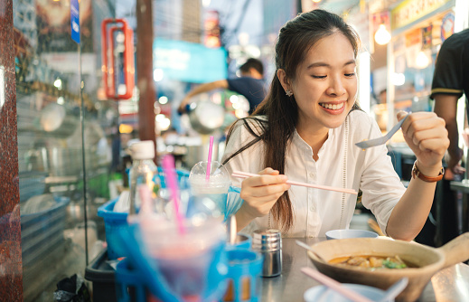 Young cheerful asia women eating chinese food style noodles in a streetfood marketplace in chinatown
