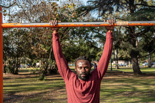 Portrait of a young man doing pull-ups on public park