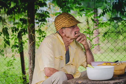 An elderly man is sitting in the garden of his house.