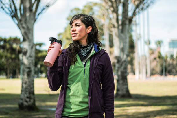 istock Young woman drinking water while looking away at public park 1616590690