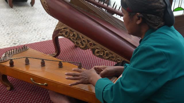 portrait senior adult wear blangkon (a west java traditional hat) in traditional clothes playing harp or zither