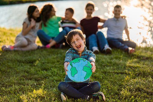 Earth planet model in boys hands outdoors. Group of kids sitting in the background