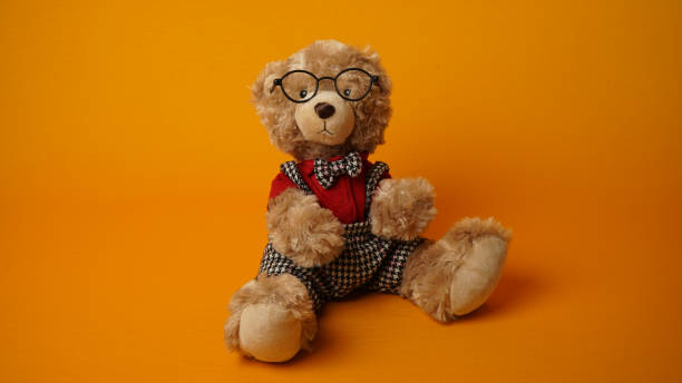 istock Sitting teddy bear in glasses on yellow background. 1616618250