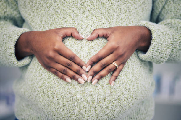 gravidez, closeup e mulher com formato de coração na barriga materna para cuidados e maternidade. saúde, zoom e mulher grávida africana mãos na barriga com um sinal de amor ou emoji para seu bebê. - bumpy - fotografias e filmes do acervo