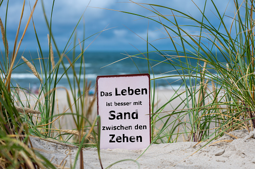 The German slogan 'das Leben ist besser mit Sand zwischen den Zehen' (life is better with Sand between the toes) in the sand dunes at the beach.