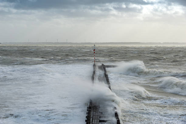 Giant waves break on a pier under a dramatic sky.
