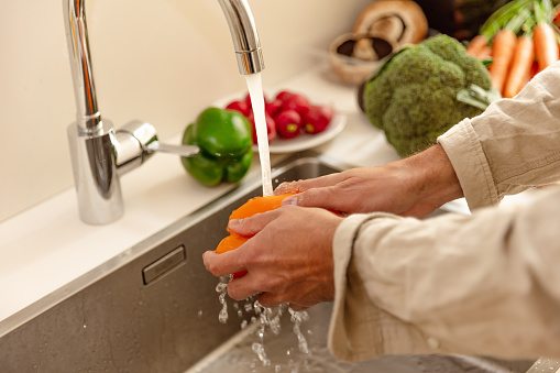 Hands of a young man washing an orange pepper in the kitchen - Preparing Raw Vegan Recipes