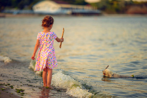 Little girl  throwing wooden stick to dog in the sea