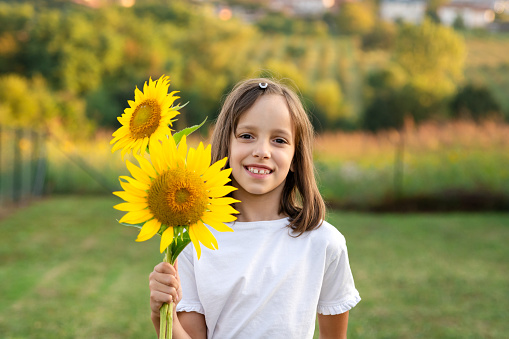 Portrait of happy girl holding sunflowers and looking at camera in nature