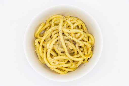 An overhead view of delicious bucatini cacio e pepe pasta in a white bowl