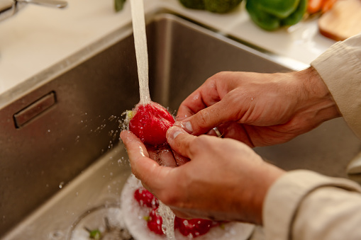 Hands of a young man washing a radish in the kitchen - Preparing raw vegan recipes