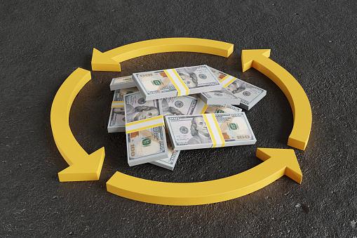 Heap of US 100 dollar stacked banknotes inside a yellow circle made of curved arrows on concrete floor. Illustration of the concept of cash flow and currency in circulation