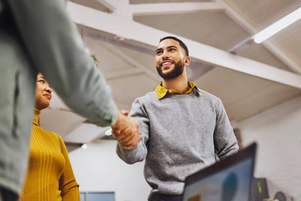 Low angle view of cheerful executive shaking hands with colleague in office Bearded executive smiling and shaking hands with new colleague in office day in the life stock pictures, royalty-free photos & images