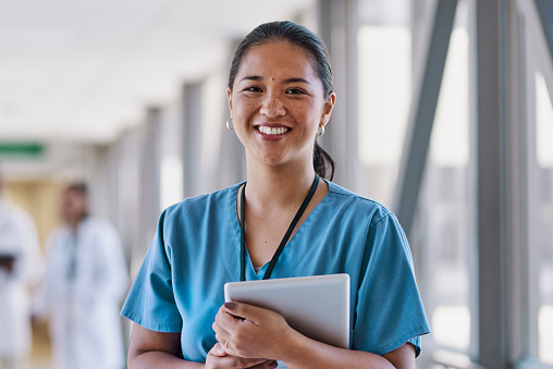 Female nurse carrying digital tablet smiling cheerfully at camera in hospital corridor