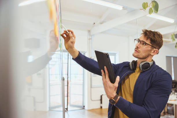istock Businessman holding digital tablet, looking at whiteboard in office 1616722195