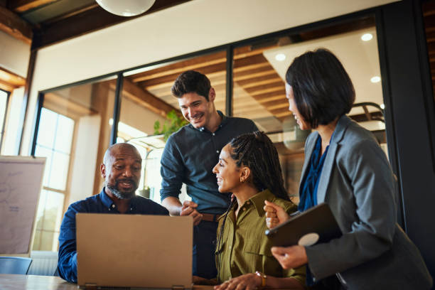 Diverse group of entrepreneurs smiling cheerfully and using laptop in boardroom