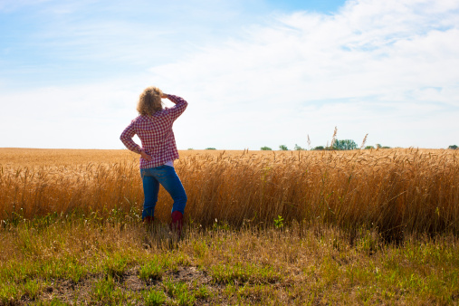 A hardworking female farmer looks out over the vast fertile open farmland with pride. Represents hardworking, 
