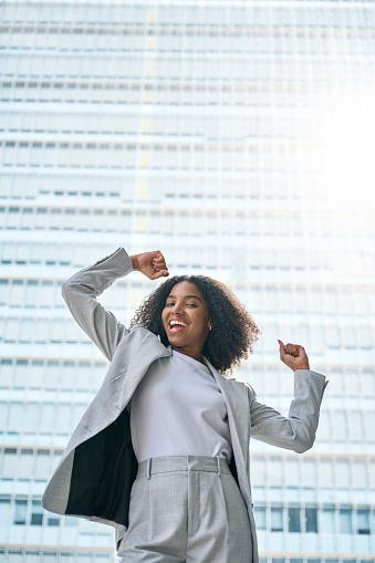 Happy excited confident professional young African American business woman office leader executive wearing suit celebrating success standing in big city street feeling strong and powerful concept.
