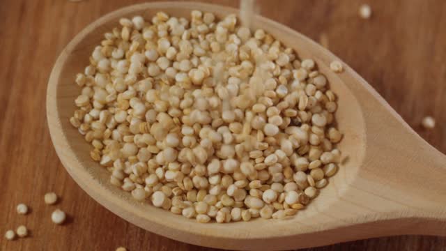 White quinoa uncooked seeds texture close up. Selective focus. Slow motion