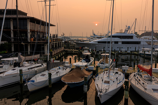 Annapolis port at sunset. Boats and yachts anchored in the harbor on the water bay as the sun sets. Canadian wildfires smog aftermath,boats on foreground, Severn River, Annapolis, MD