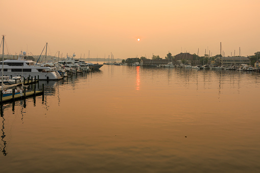 Smoggy Severn River's waterfront delight at sunset, Canadian fires aftermath: boats and yachts anchored in the harbor on the water bay of Annapolis, Maryland