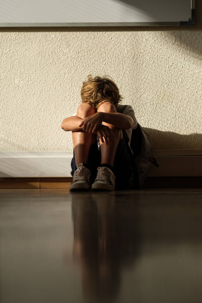 istock Upset boy embracing knees of floor in classroom 1616813106