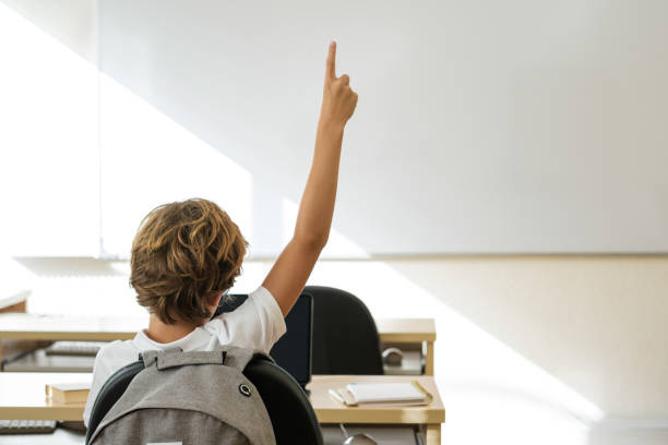 istock Schoolboy putting hand up in classroom at school 1616815850