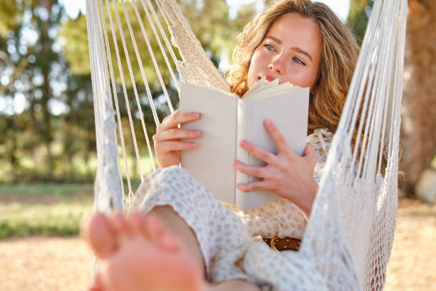 istock Dreamy female with book chilling on hammock in garden 1616840475