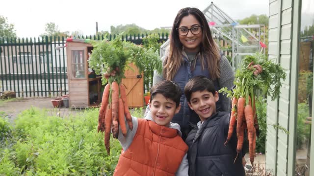 A young mother and two boys holding freshly dug vegetables at a local community garden