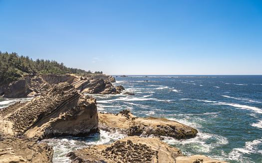 Rugged Rocky shoreline landscape along the Southern Oregon Coast with waves breaking on the jagged rocks and a bright blue sky with copy space.