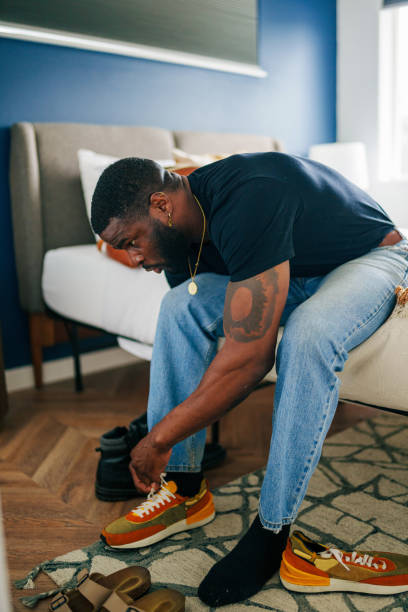 istock Man sits on edge of bed, putting shoes on 1616872414